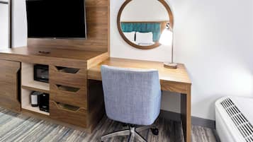 Una camera d'albergo con una scrivania in legno, una televisione, uno specchio tondo, una sedia e un termosifone.