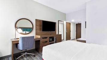 A hotel room with a bed, a desk with a chair, a television, a mirror, and a microwave.