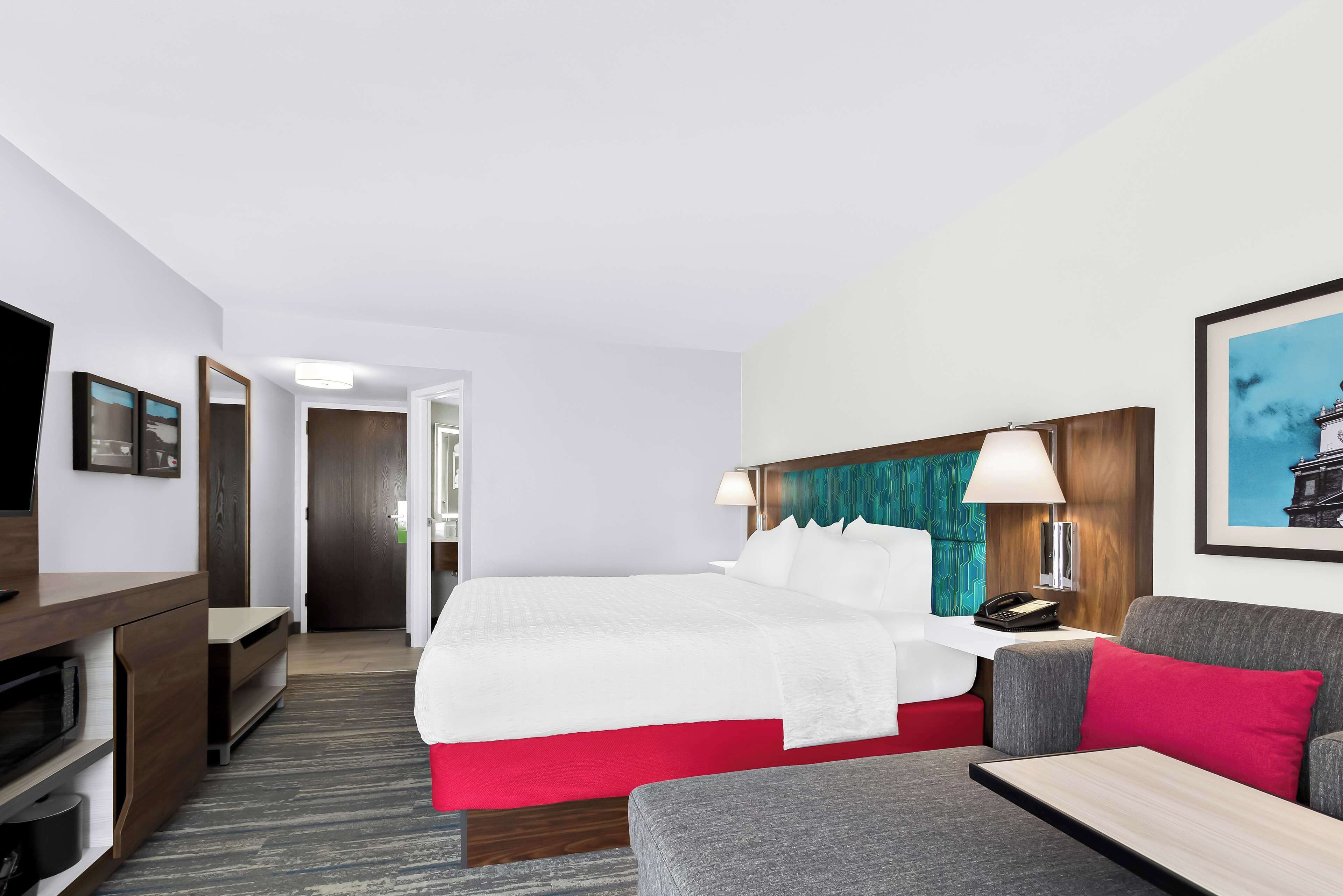Una habitación de hotel con cama, escritorio, televisor y sofá.