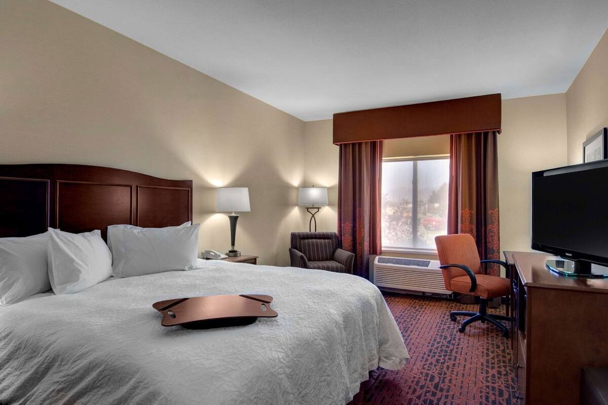 Une chambre d’hôtel comprenant un lit, un bureau avec un ordinateur, une chaise, une lampe et un téléviseur.