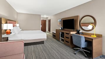 A hotel room with a large bed, a desk with a chair, a TV, a desk lamp, and a mirror.