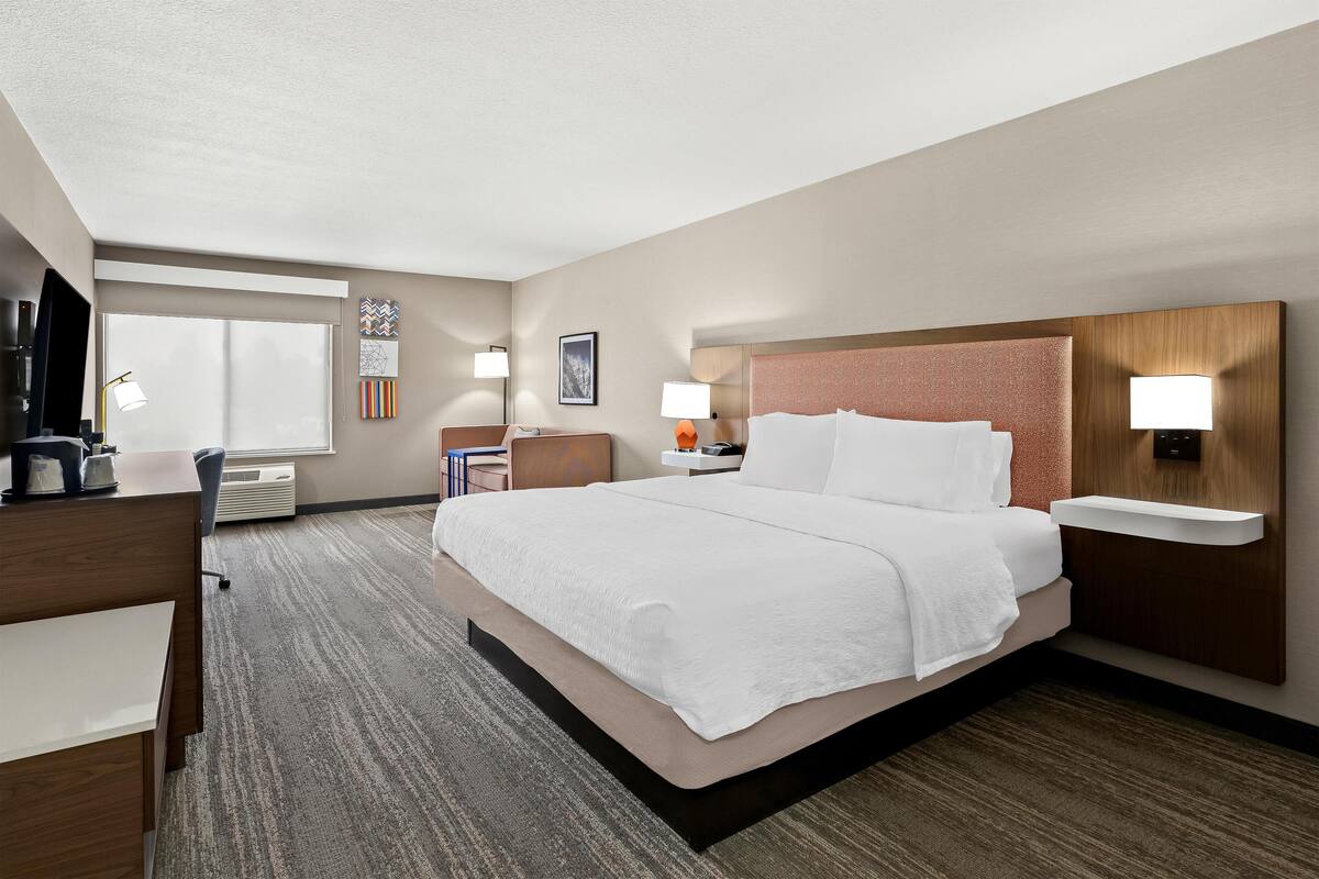 Une chambre d’hôtel avec un grand lit, un bureau, une chaise, une télévision et une fenêtre.