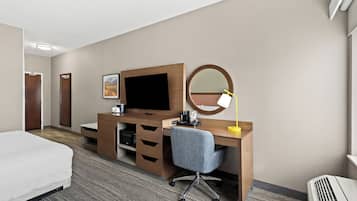 Een hotelkamer met een bed, een bureau met een computer, een bureaulamp, een spiegel en een televisie.