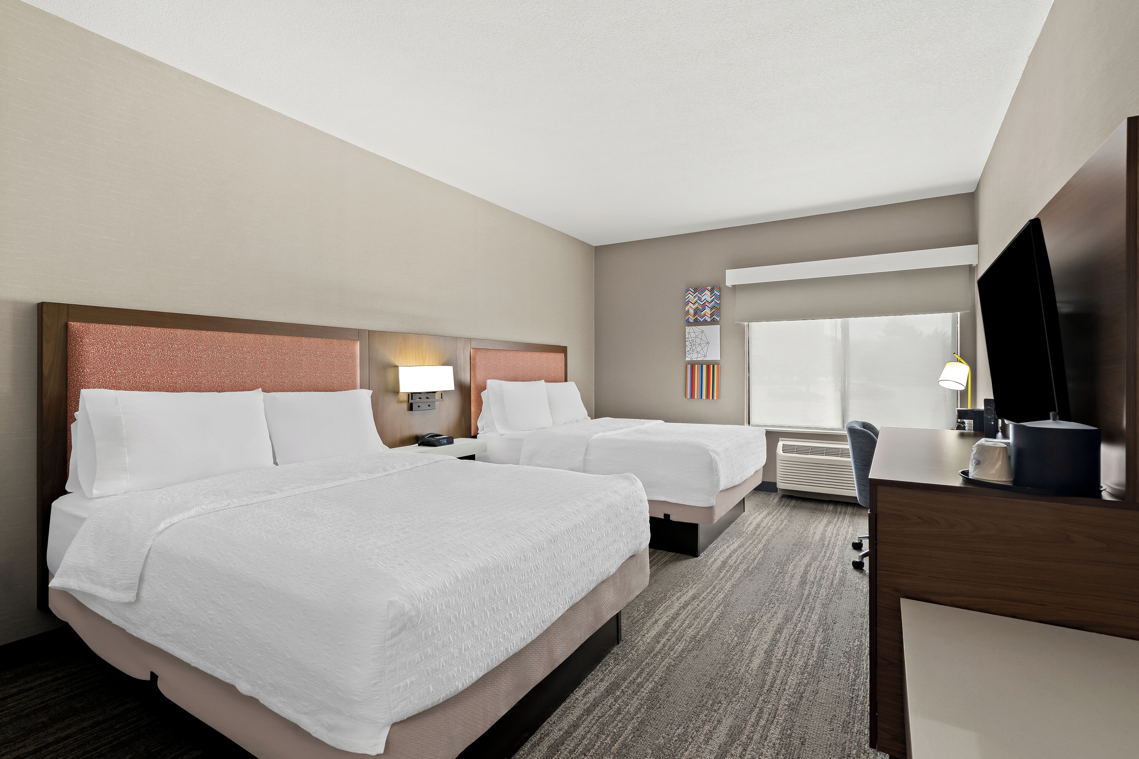 A hotel room with two beds, a desk, a TV, and a window with a view.