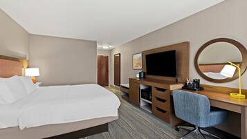 A hotel room with a bed, a desk, a chair, a television, a mirror, and a lamp.