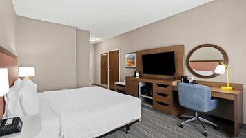 A hotel room with a bed, a desk with a computer, a TV, a mirror, and a lamp.