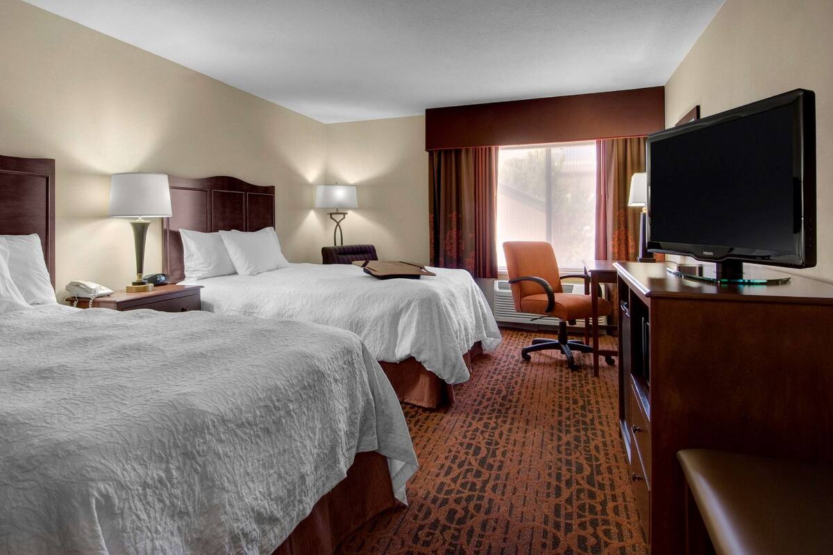 Une chambre d’hôtel avec deux lits, un bureau équipé d’une télévision, une chaise, une lampe et un téléphone.