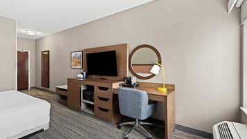 Quarto de hotel com cama, escrivaninha com computador, cadeira, abajur, espelho e televisão.