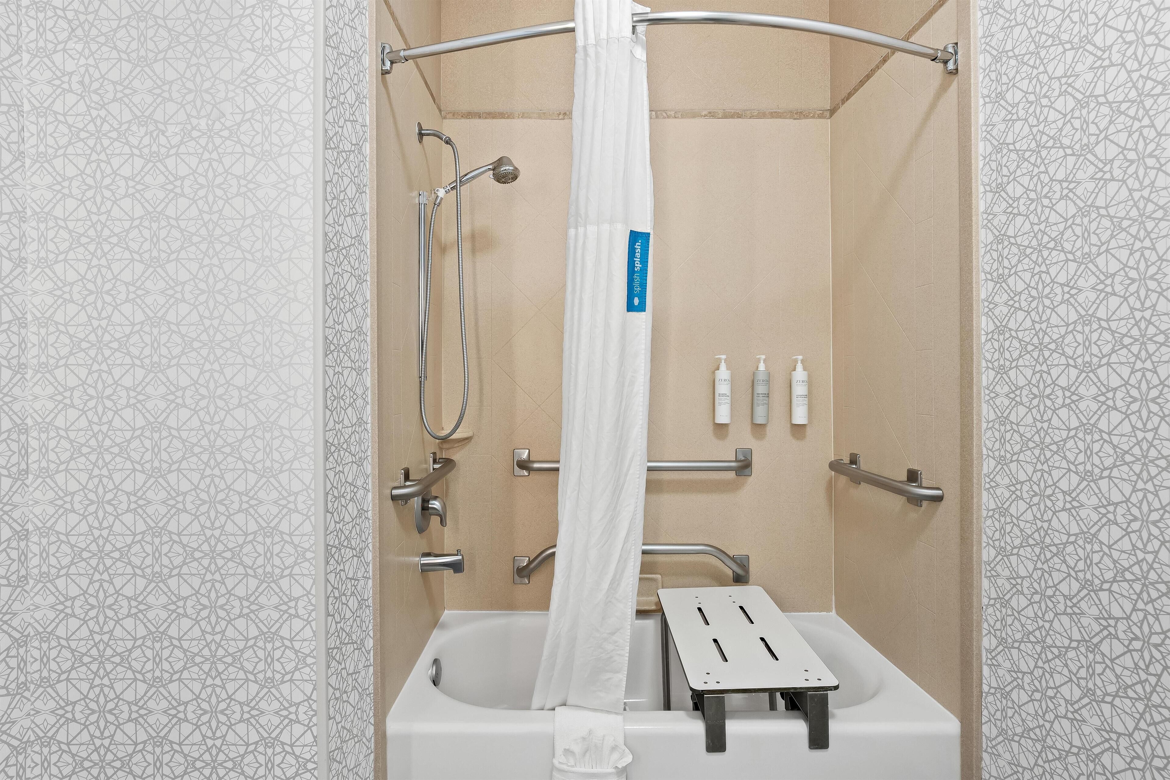 A modern bathroom with a shower, grab bars, and a white towel.