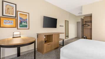 A hotel room with a bed, a desk with a chair, a TV mounted on the wall, and a mirror.