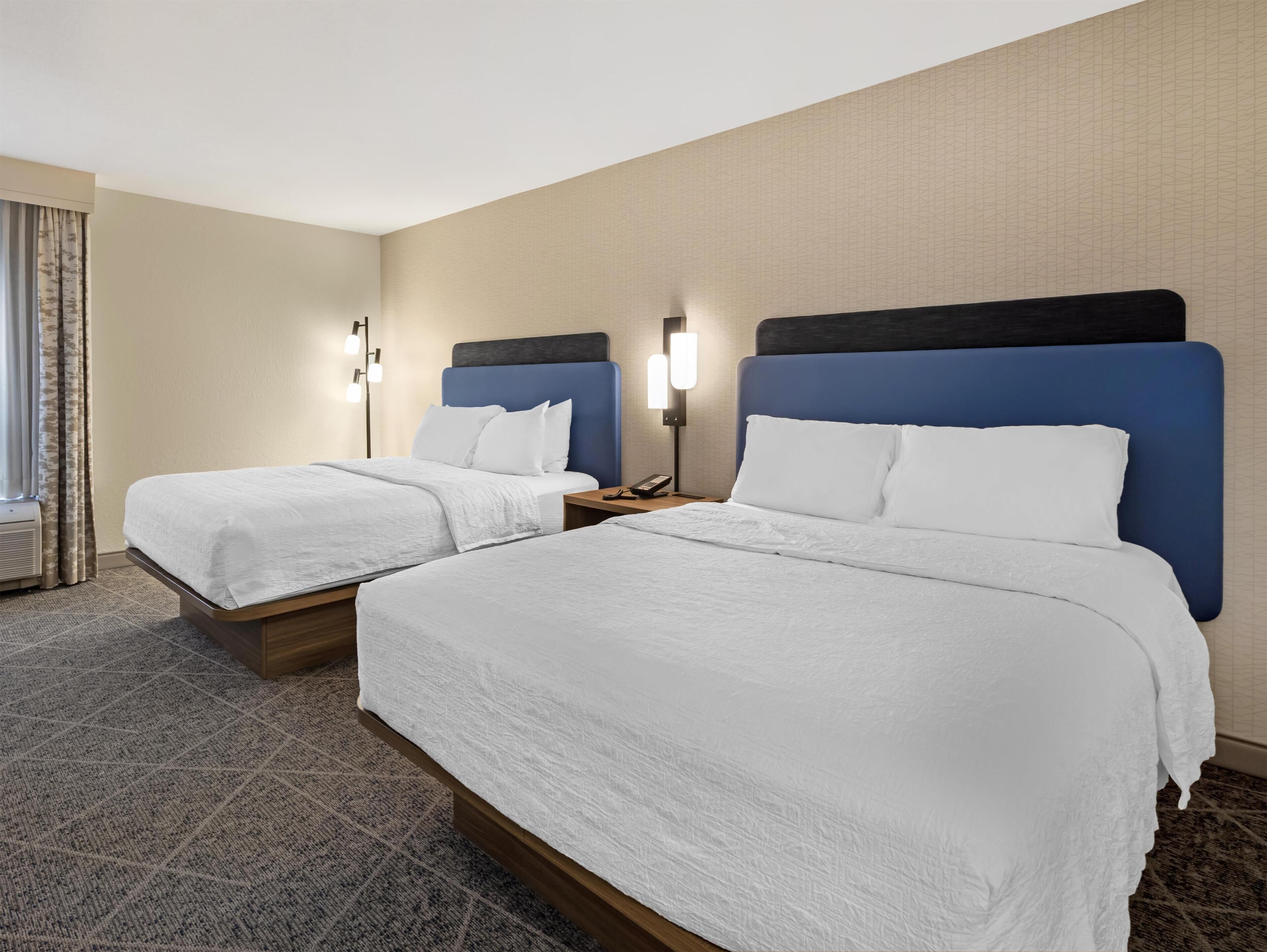 Ein Hotelzimmer mit zwei Betten, einem Nachttisch mit Telefon und einer Wandlampe.