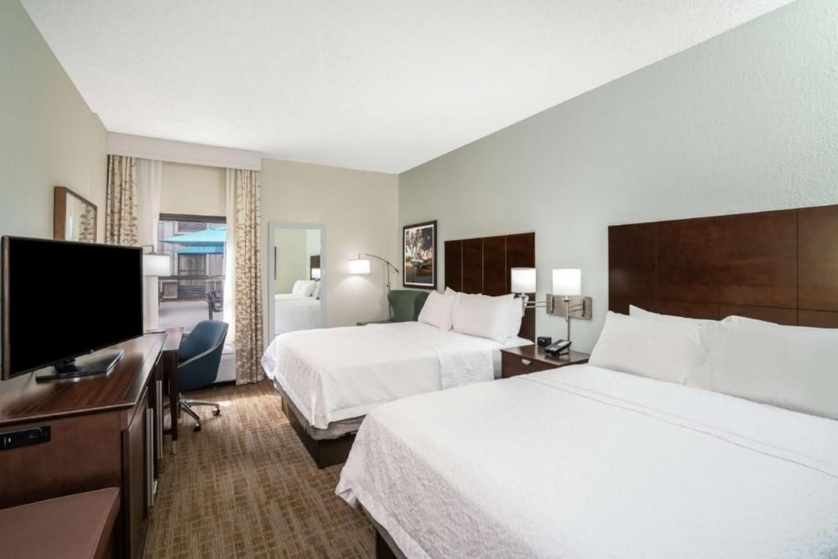 A hotel room with two beds, a desk with a TV, a chair, and a view of the outside.