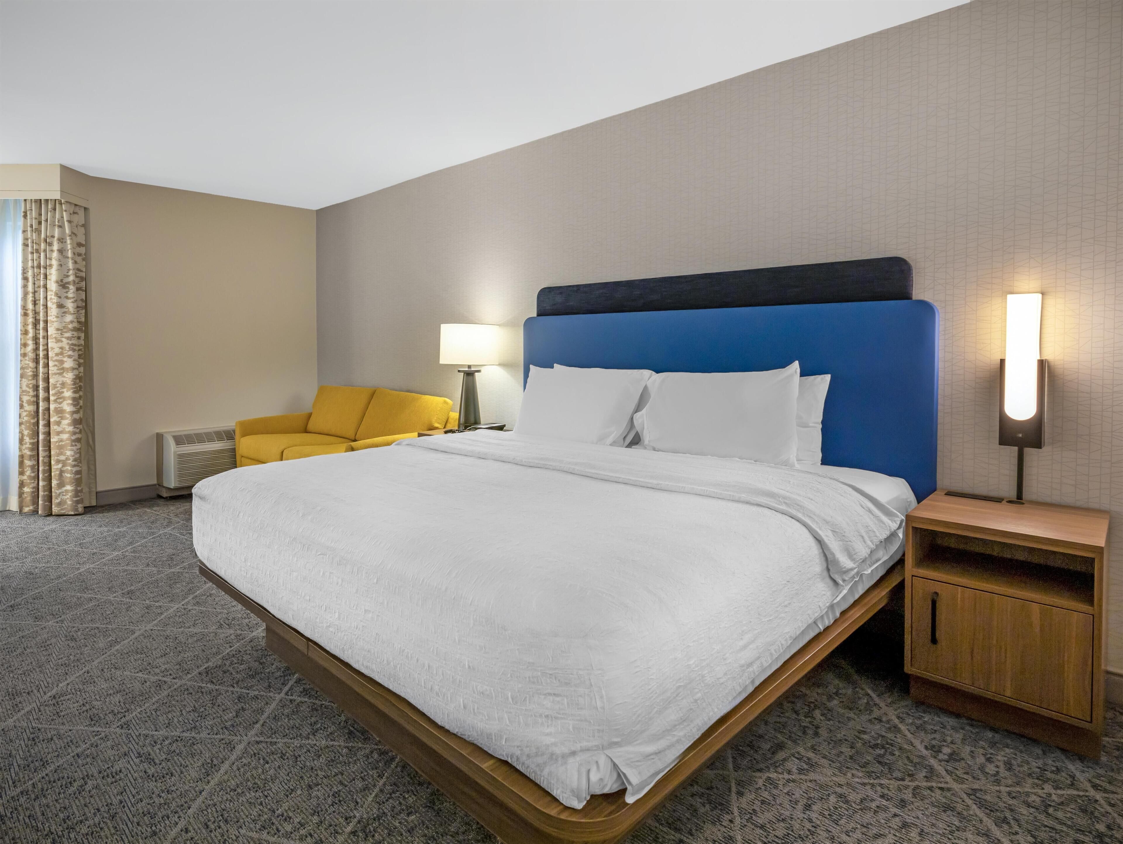 A hotel room with a large bed, a sofa, a nightstand, a lamp, and a wall with a textured pattern.