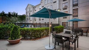An outdoor patio area with tables and chairs, a large potted plant, and a building in the background. - Hampton Inn & Suites Nashville/Franklin (Cool Springs) (Franklin)