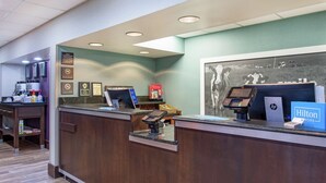 A hotel reception desk with a digital kiosk, a HP laptop, and a sign for Hilton Honors. - Hampton Inn Cullman (Cullman)