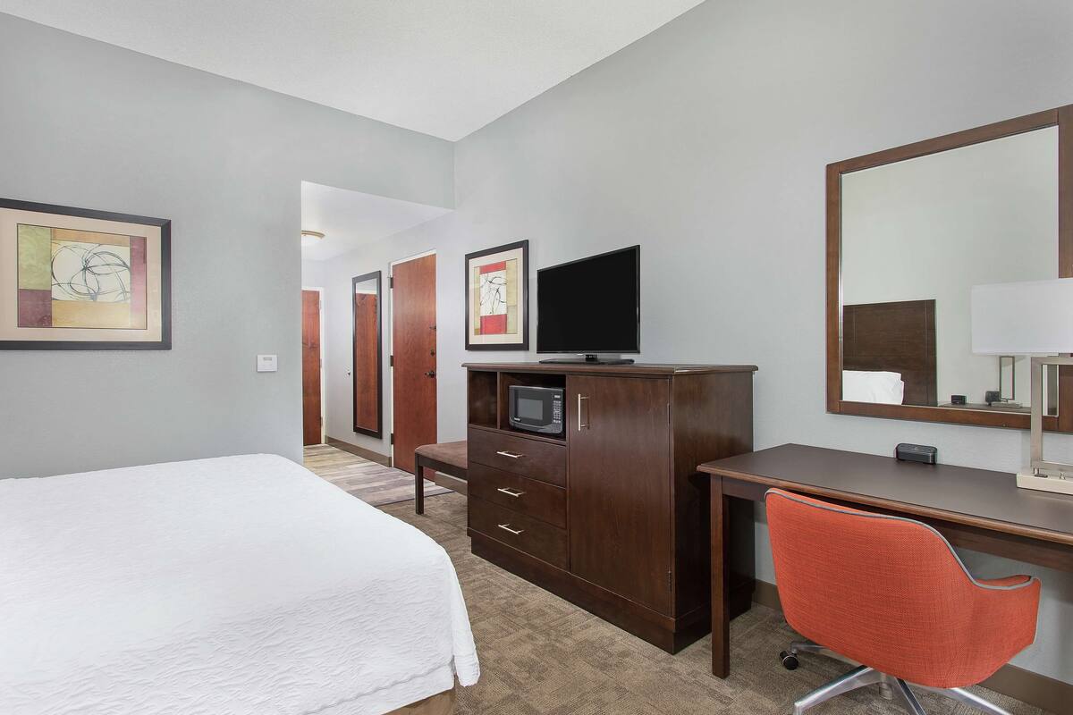 Habitación de hotel con cama, escritorio con computadora, silla, televisor y microondas.
