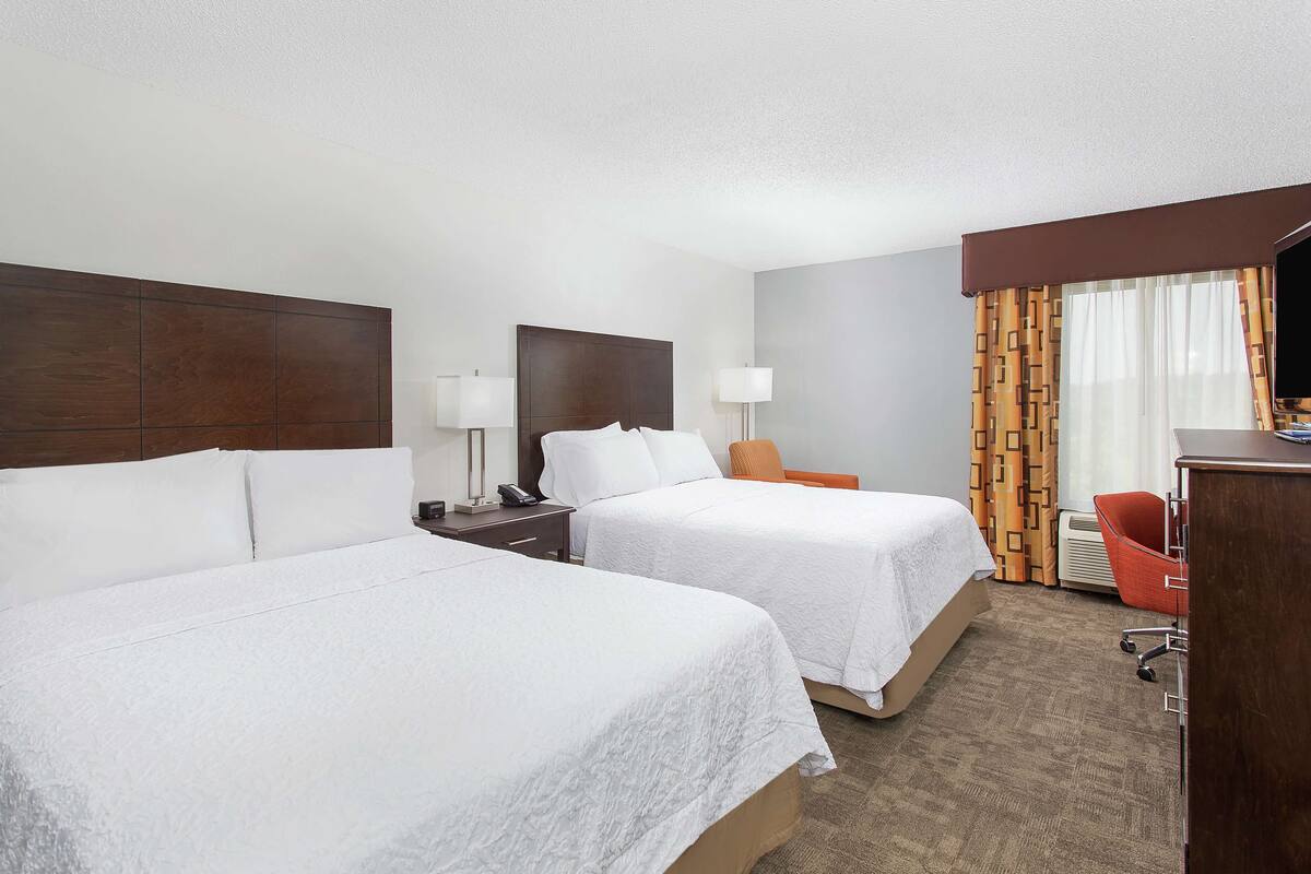 Habitación de hotel con dos camas, un escritorio, una silla y un televisor.