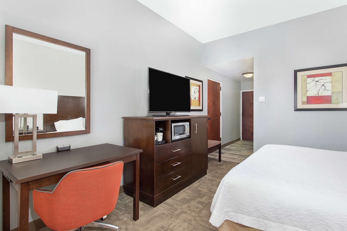 Una habitación de hotel con cama, escritorio, silla, televisor, microondas y armario.