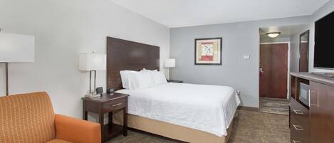 A hotel room with a bed, a desk with a lamp, a chair, and a television.