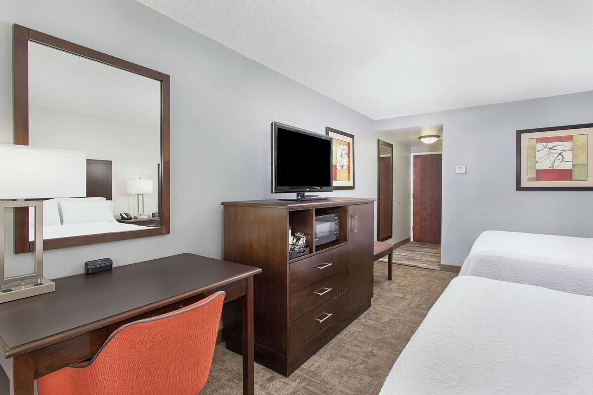 A hotel room with a bed, a desk with a chair, a television, a dresser, and a mirror.