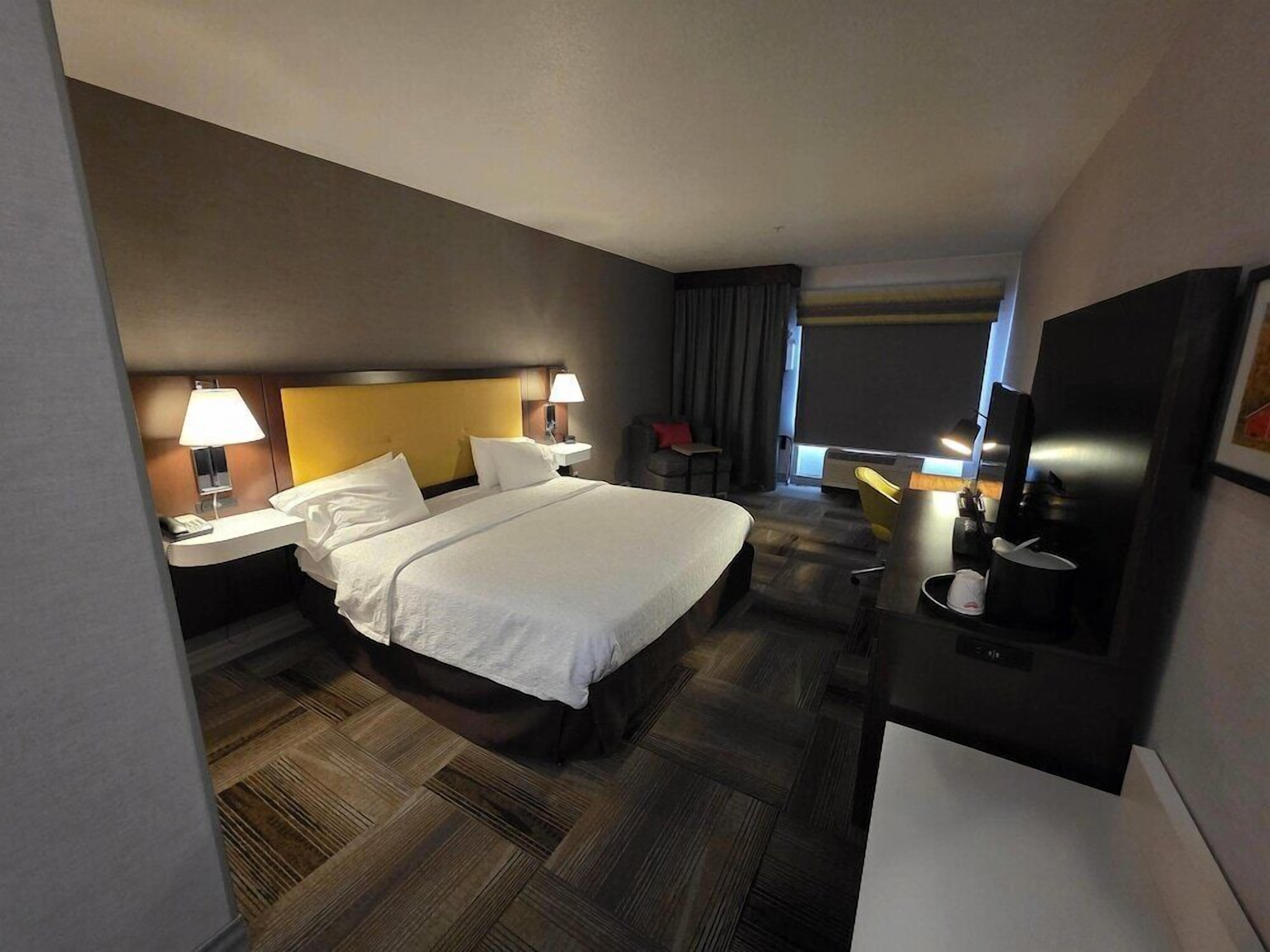 A hotel room with a large bed, bedside tables with lamps, a desk with a chair, and a television.