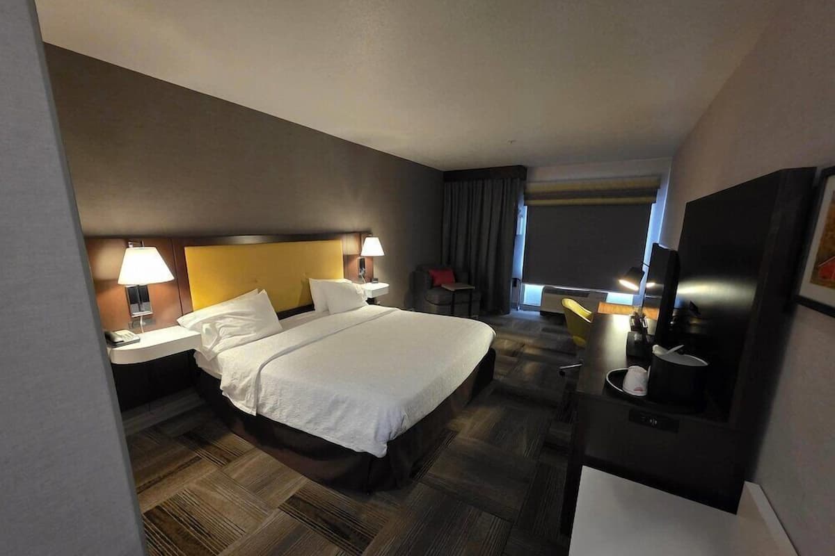 A hotel room with a large bed, bedside tables with lamps, a desk with a chair, and a television.