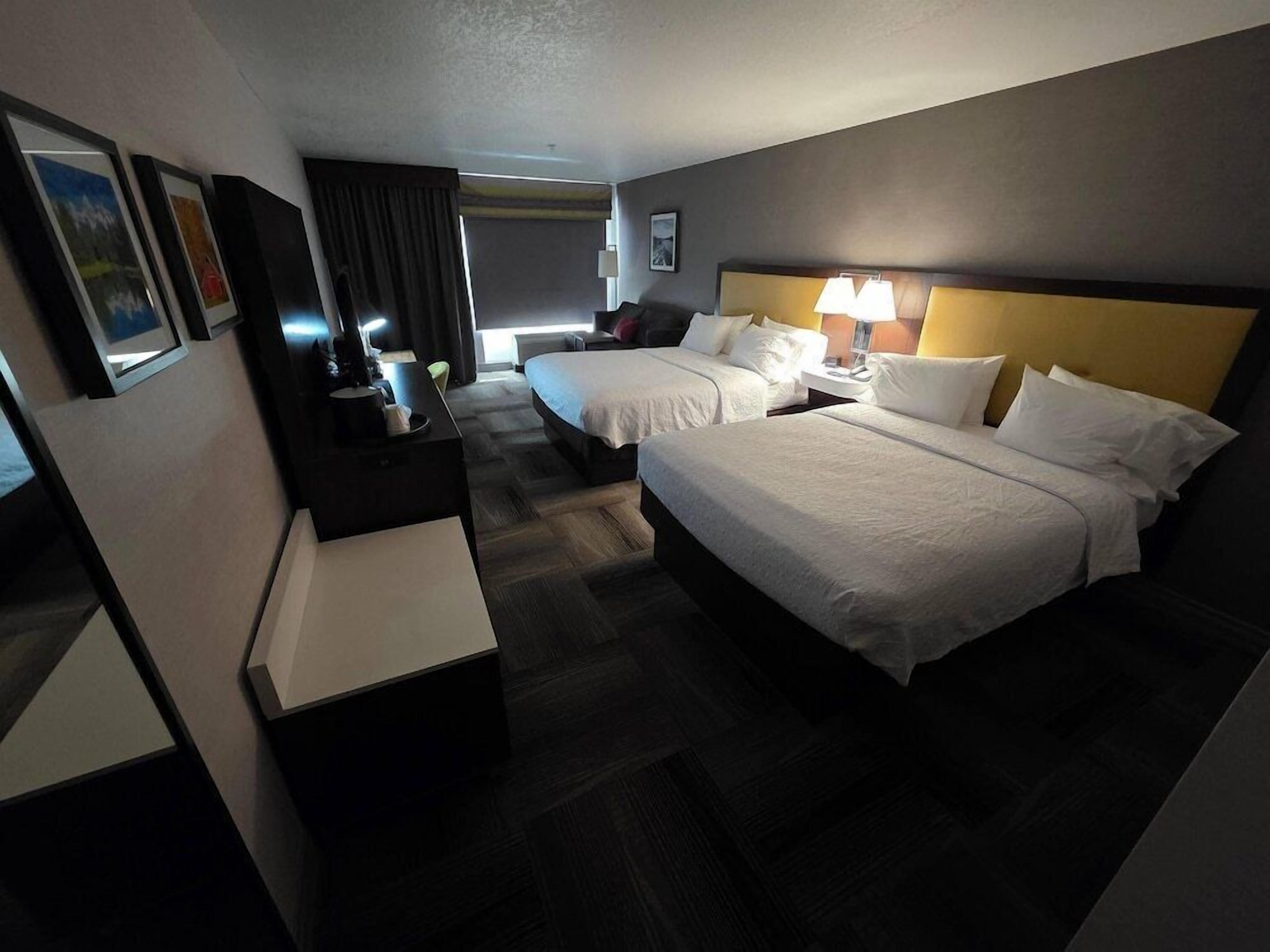 A hotel room with two beds, a desk, a chair, a lamp, and a picture on the wall.