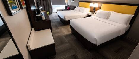 A hotel room with two beds, a desk, a chair, a lamp, and artwork on the walls.