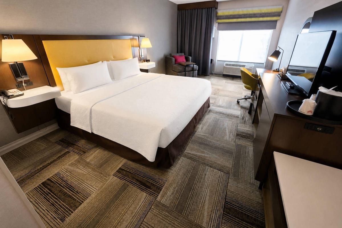 A hotel room with a large bed, bedside lamps, a desk with a computer, a chair, and a TV.