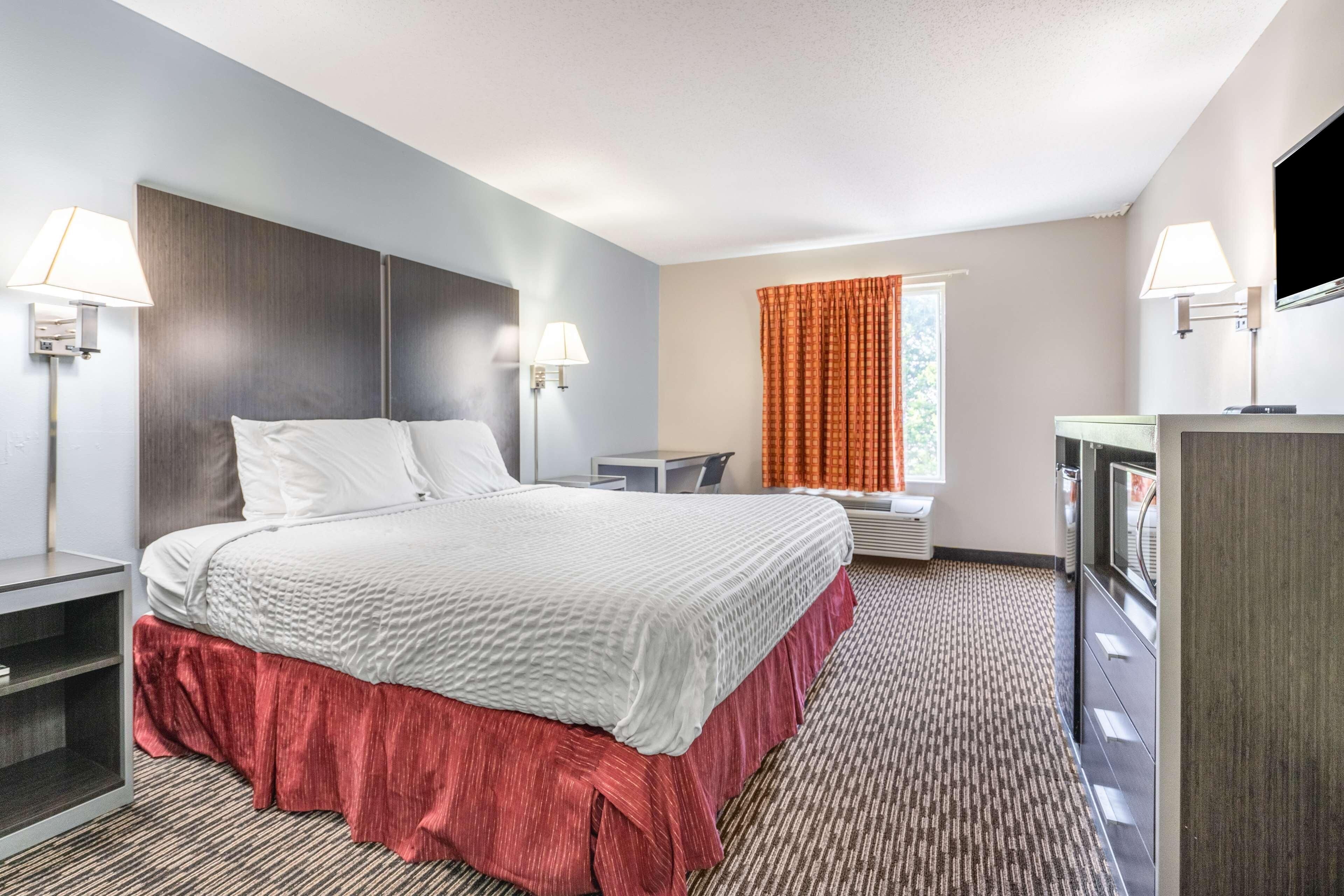 A hotel room with a bed, bedside tables, a desk, a TV, and a window with curtains.