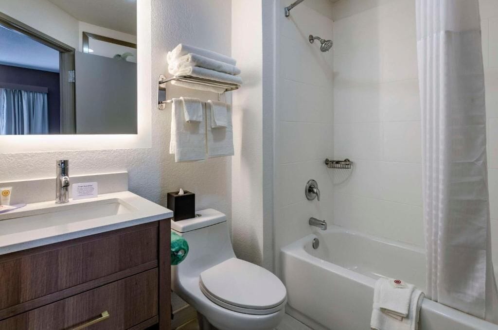 A bathroom with a white sink, toilet, and bathtub. There is a towel rack with folded towels above the toilet.
