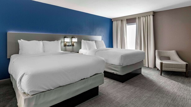 Habitación de hotel con dos camas, una silla y un ventanal con cortinas.