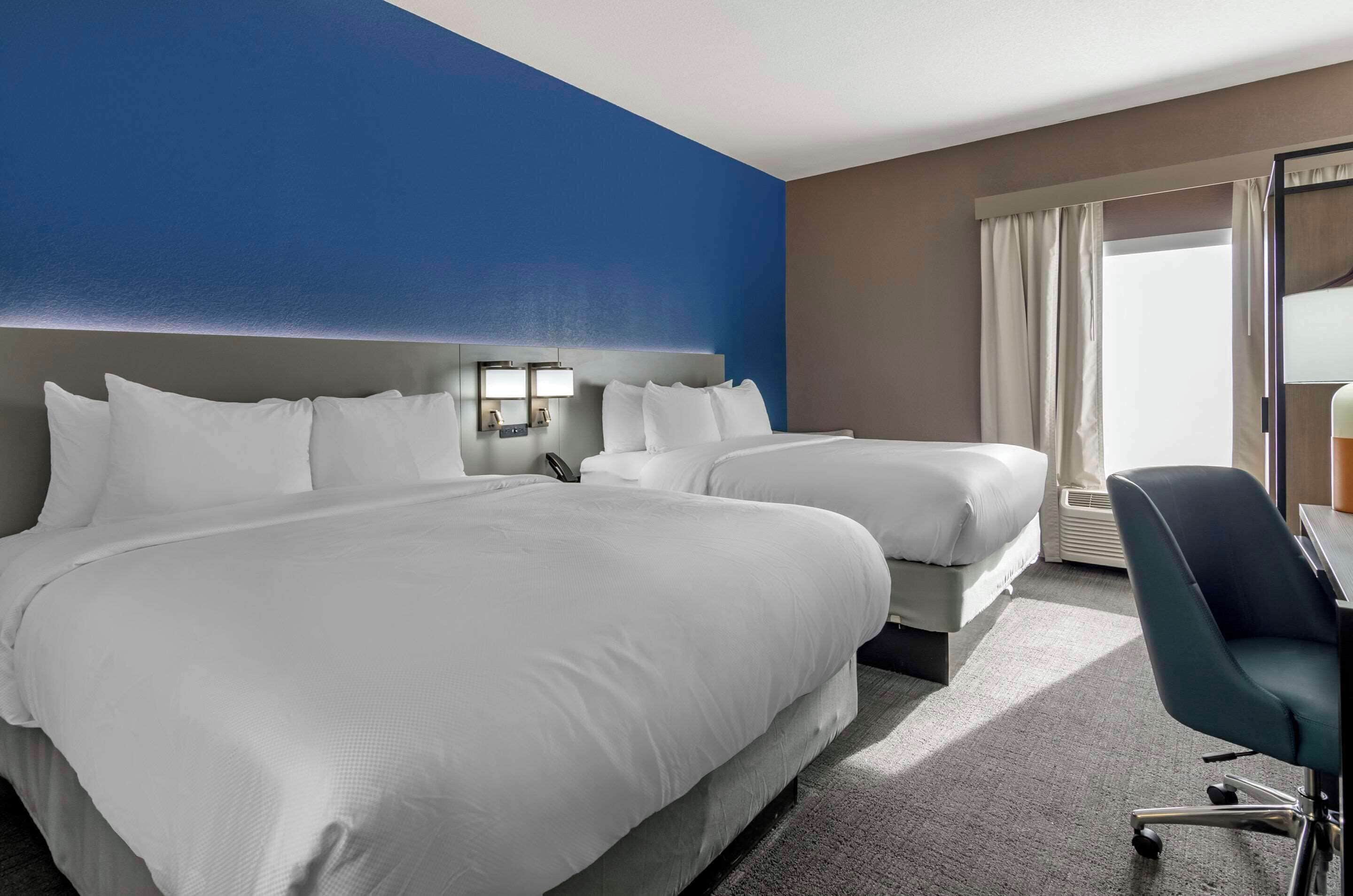 A hotel room with two beds, a desk, and a chair.