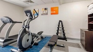 Un gimnasio con equipo de cardio, una banca y mancuernas.