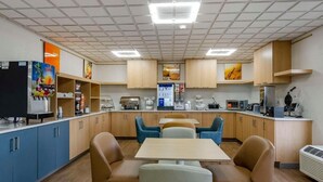 Una cocina moderna con armarios azules, un refrigerador, un microondas y una cafetera. Hay dos mesas con sillas.