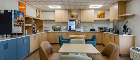 Una cocina moderna con armarios azules, un refrigerador, un microondas y una cafetera. Hay dos mesas con sillas.