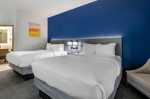A hotel room with two beds, a blue accent wall, and a small seating area.