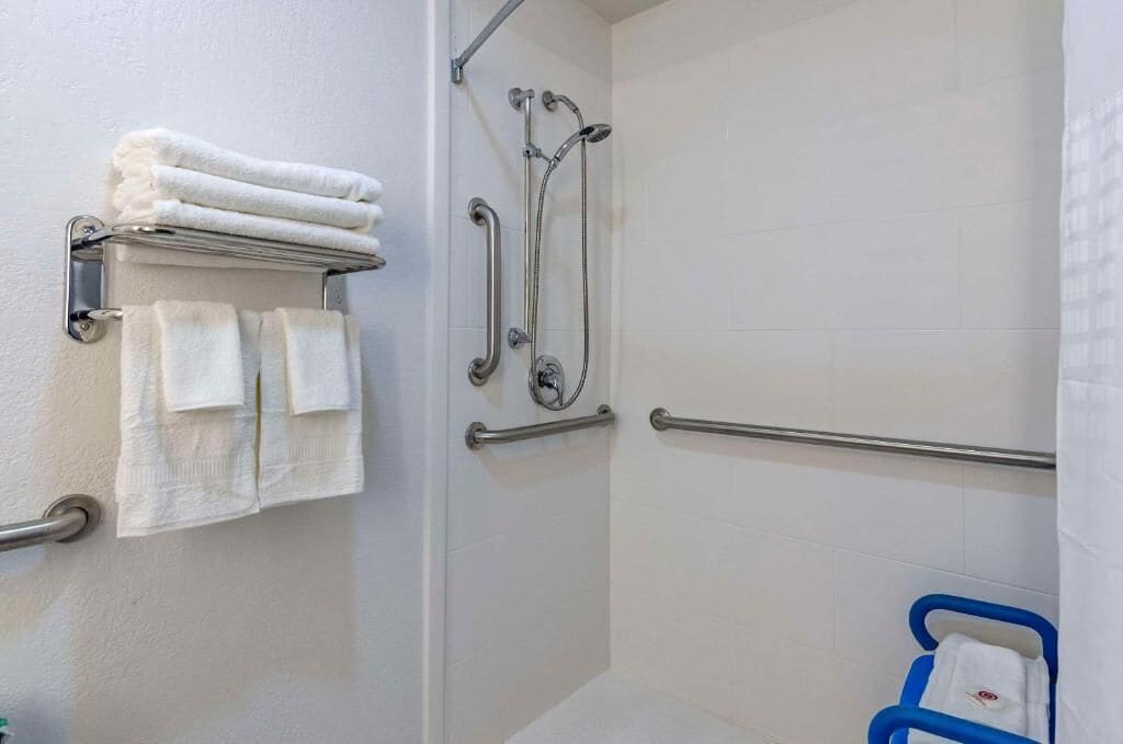 A bathroom with a shower, grab bars, and a towel rack with folded towels.