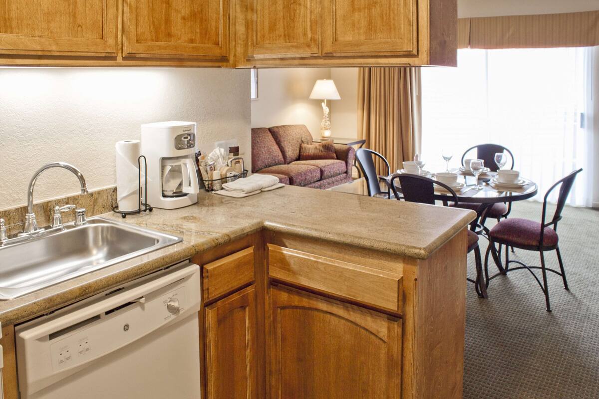 A kitchen with wooden cabinets, a built-in dishwasher, a coffee maker, and a dining area with a table set for two.