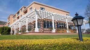 Un immeuble à plusieurs étages doté d’un espace extérieur couvert, qui pourrait être un hôtel ou un bâtiment public, avec une pelouse bien entretenue et un lampadaire au premier plan.