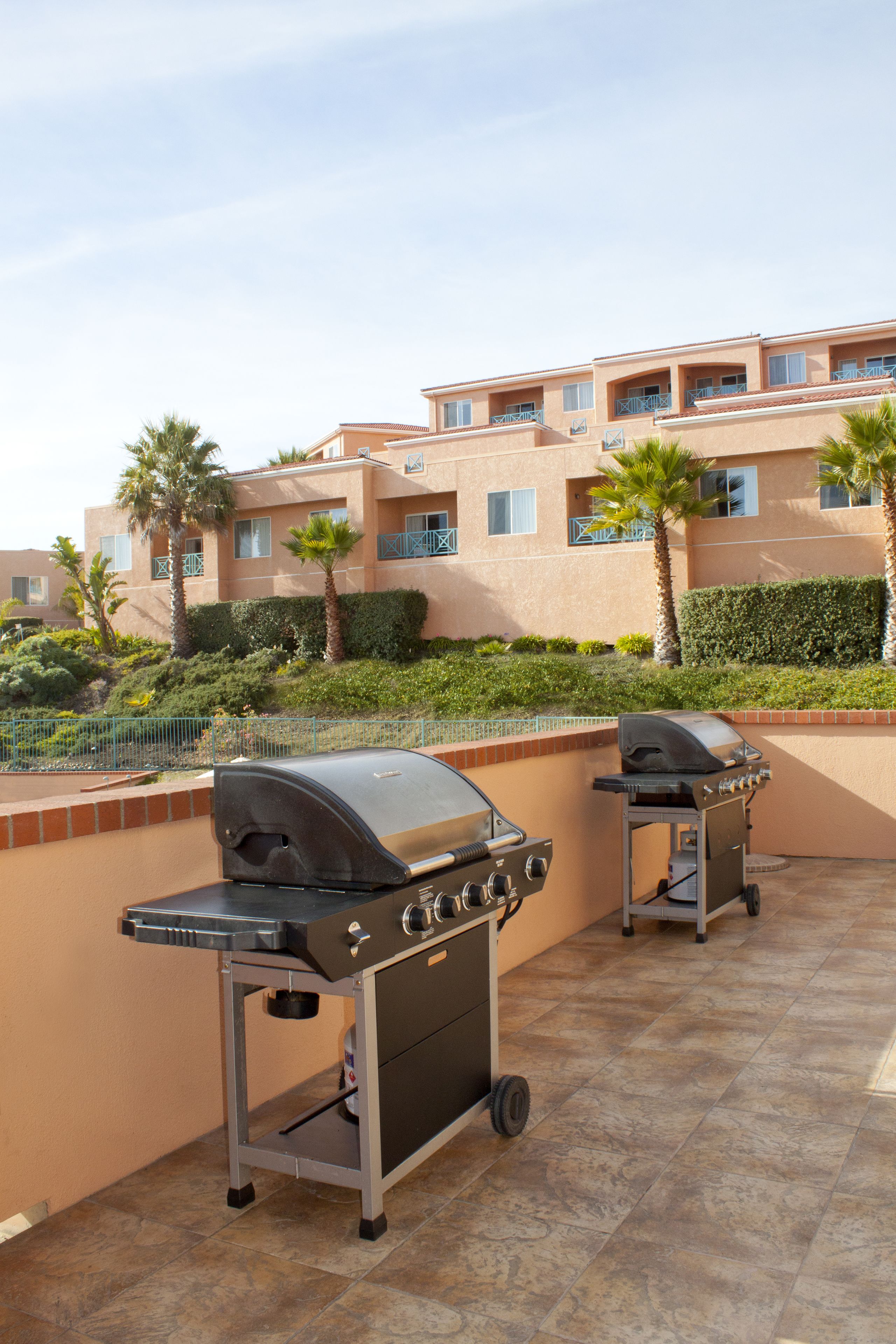 Two portable grills on a patio with a view of a multi-story building and palm trees.
