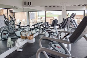 A gym with various exercise equipment, a fan, and a view of outdoor seating.