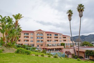 A multi-story hotel with balconies, a swimming pool, and palm trees.