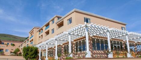 A hotel with a modern architectural design, featuring a covered outdoor area with a patterned roof, multiple balconies, and a well-maintained lawn.