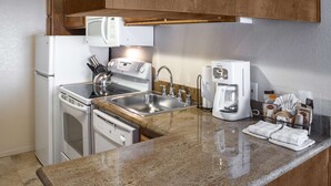 Une cuisine compacte équipée d’un réfrigérateur, d’une cuisinière, d’un four à micro-ondes, d’un évier et d’une machine à café.