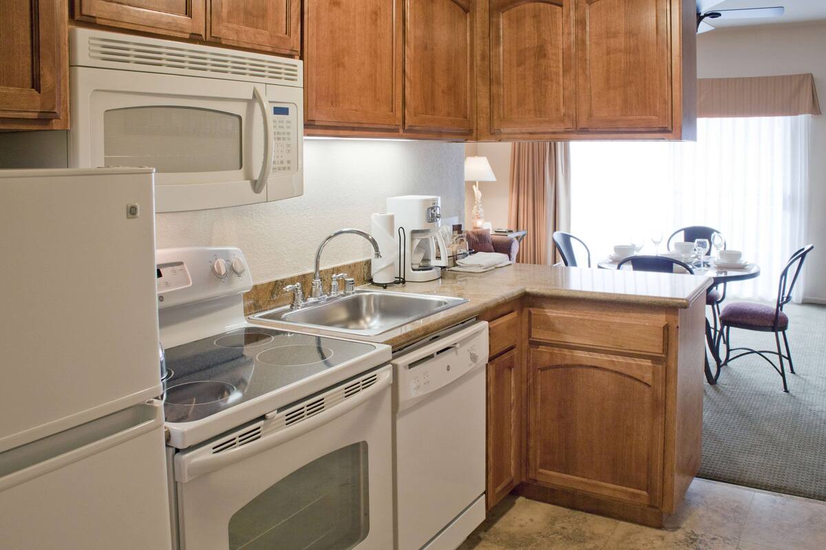 A kitchen with a microwave, stove, sink, and dishwasher. There is a dining area with a table and chairs.
