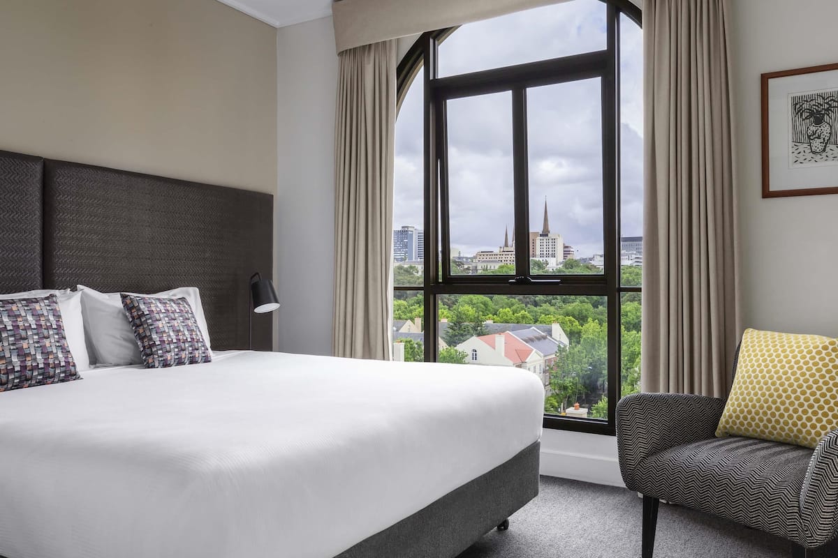 Een hotelkamer met een groot bed, uitzicht op de stad en een stoel met een gestreept kussen.
