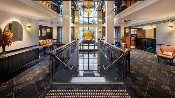 A spacious hotel lobby with a central staircase, multiple seating areas, and a reception desk. - Mantra on Jolimont Melbourne (East Melbourne)