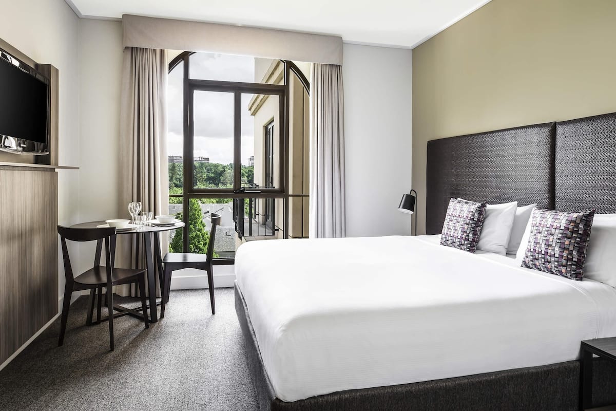 Een hotelkamer met een bed, een bureau, een stoel, een televisie en een raam met gordijnen.