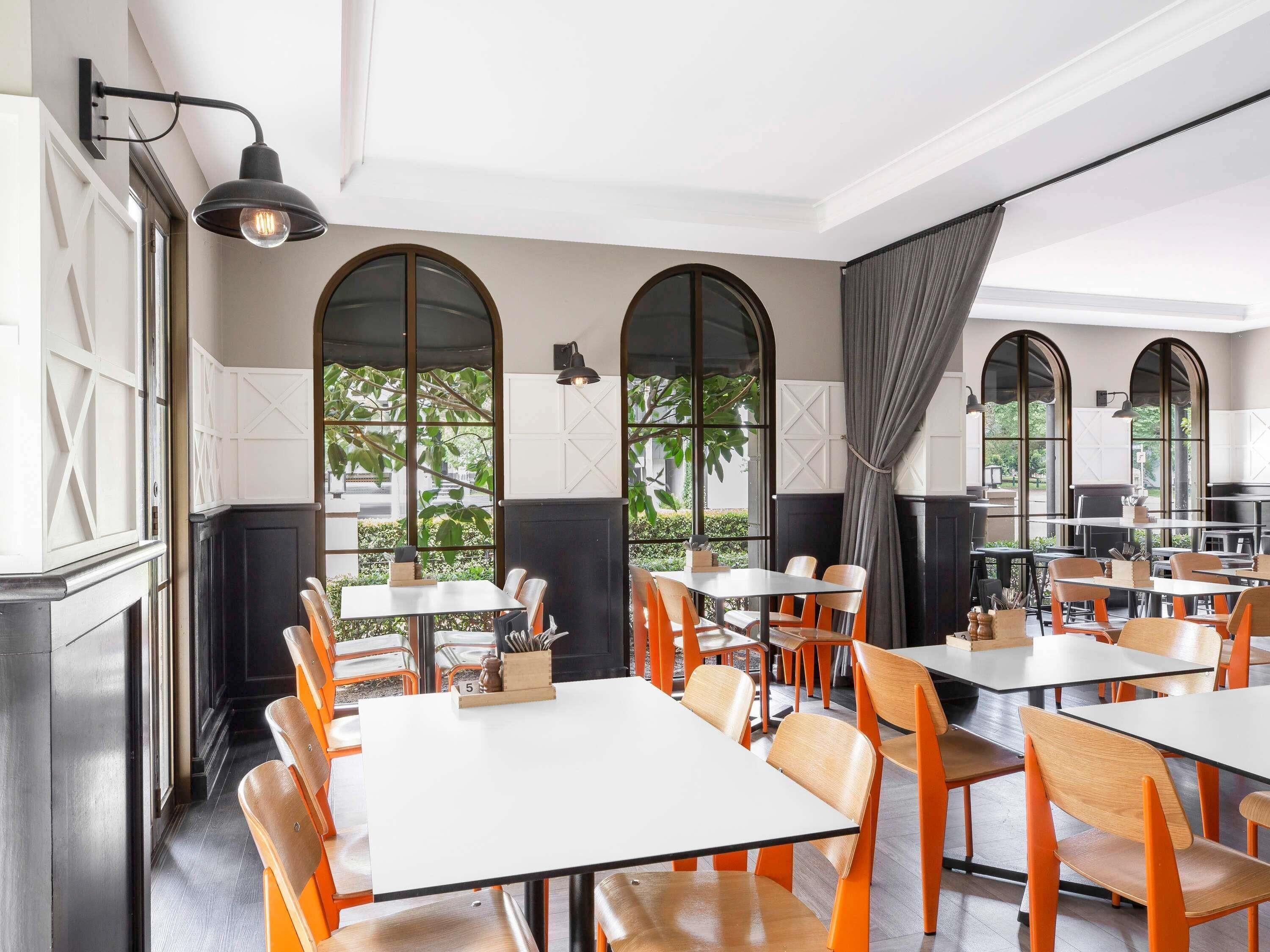 A restaurant interior with tables and chairs, large windows, and a fireplace.